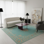 A styled living room scene featuring a large turquoise and beige patterned area rug on a light wood floor, with a cream curved sofa, dark wood coffee table, black side table and lamps, and a gray armchair.