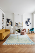 Modern living room with a yellow sofa, patterned rug, and abstract art on the walls.