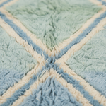 Close-up of a plush textured rug with a geometric diamond pattern in light blue, mint green, and cream.