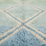 Close-up of a soft, textured rug with a geometric diamond pattern in light blue and cream.