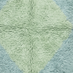 A close-up of a textured, looped fabric product, likely a blanket or throw, featuring a central pale sage green diamond shape bordered by light blue sections.
