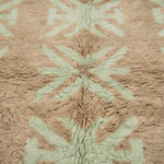 Close-up of a plush textured rug with a geometric pattern in light beige and pale sage green.