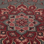 Close-up of a traditional patterned rug with a central medallion design in red, dusty pink, gray, and dark brown tones.