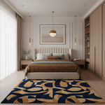 A modern bedroom interior with a bed dressed in brown and gray bedding, flanked by matching nightstands and a large abstract area rug in navy and beige. A cream upholstered headboard and matching footboard are visible, with a framed abstract print above the bed, pendant lights, built-in wood shelving, and sheer curtains on the left.