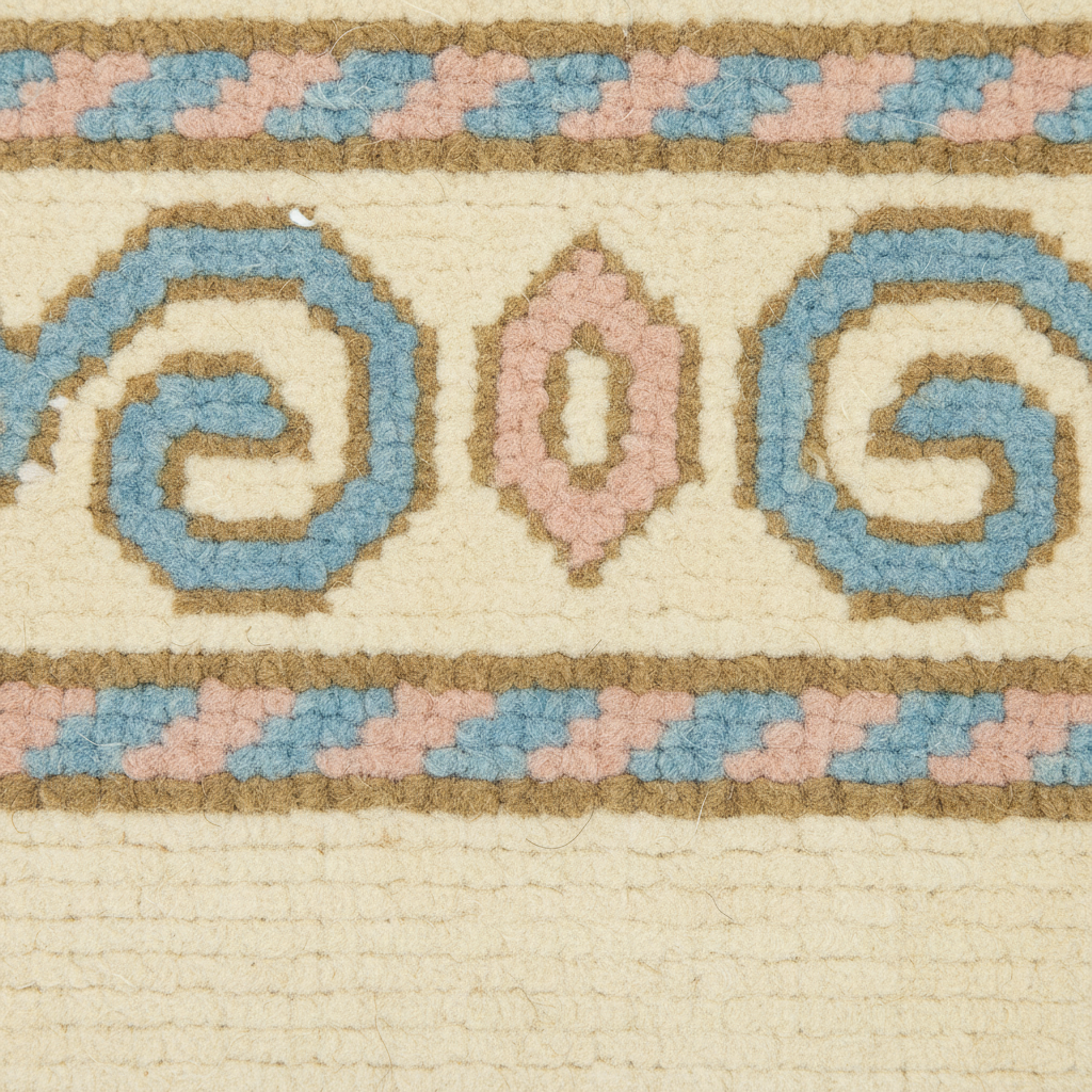 Close-up of a woven rug or textile with a cream base and a decorative border featuring blue, blush pink, and tan geometric and spiral motifs.