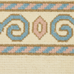 Close-up of a woven rug or textile with a cream base and a decorative border featuring blue, blush pink, and tan geometric and spiral motifs.