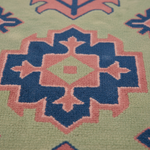 Close-up of a textured rug with a geometric medallion pattern in sage green, dusty pink, and navy blue.