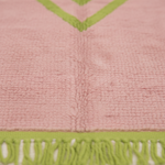 Close-up of a pink textured fabric item with a lime green chevron pattern and matching fringed trim along the bottom edge.