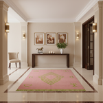 A pink rectangular area rug with green geometric line patterns and fringe, displayed in a luxurious beige entryway with classical columns, wall sconces, and a console table.