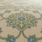 Close-up of a patterned rug with a central floral medallion in sage green, dusty blue, and cream, with a softly blurred foreground and background.