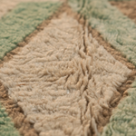 Close-up of a plush shag rug with a geometric diamond pattern in beige, light brown, and sage green.