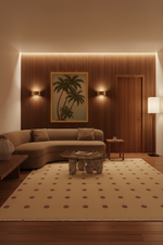 A modern living room scene with a curved beige sofa, a patterned beige rug, a wooden slatted accent wall, wall sconces, a framed palm tree painting, and warm ambient lighting.