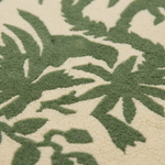 Close-up of a textured rug with a green botanical leaf pattern on a warm cream background.