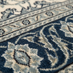 Close-up of a patterned area rug with a deep navy blue and cream floral motif, showing the detailed texture of the pile.