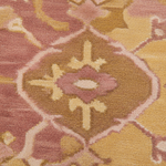 A close-up of a plush area rug with a traditional medallion pattern in dusty pink, mustard yellow, tan, and cream.