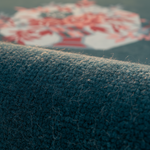 Close-up of a dark blue-gray textured carpet or rug surface with a blurred red and white patterned area in the background.
