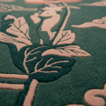 Close-up of a textured rug featuring a raised botanical pattern in dark teal green and dusty pink.