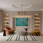 A modern living room interior with a large framed turquoise artwork hanging on the wall above a round stone coffee table. The room includes an orange armchair, a mustard ottoman, black side tables, a patterned rug, shelving, and a chandelier.