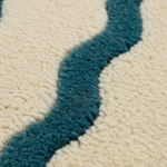 Close-up of a textured rug with a wavy, organic pattern in deep teal blue and cream.