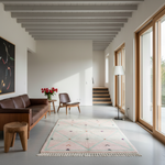 A modern living room interior with a brown leather sofa, wooden stool, mid-century chair, white floor lamp, and a light pink patterned rug on a concrete floor. Large wood-framed windows line the right wall, and a staircase is visible in the background.