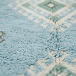 Close-up of a plush, textured rug with a light blue and cream geometric pattern.