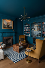 Cozy living room with blue rug, blue walls, yellow armchairs, and a bookshelf.
