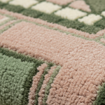 Close-up of a plush, high-pile rug with a geometric patchwork design in dusty pink and sage green.