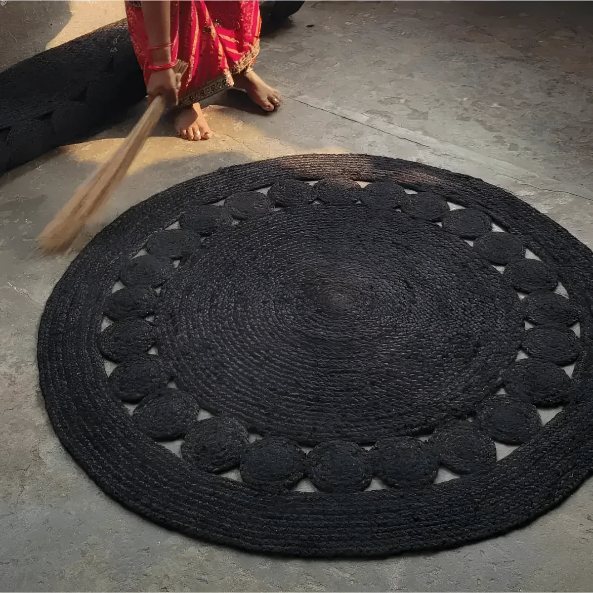Black circular rug on a concrete floor with a person using a broom.