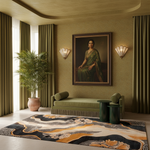 A styled interior room with olive green curtains, a matching green chaise lounge, a large abstract area rug in black, gold, and cream, and a framed portrait of a woman in a green sari on the wall.