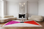 A modern living room featuring a large geometric area rug with bright pink, red, orange, and black color blocks on a cream background. The room is styled with two curved beige sofas, a marble coffee table, and a white fireplace in the background.
