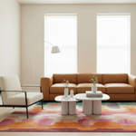 A modern living room scene with a tan leather sofa, cream armchair, two white coffee tables, a tall white floor lamp, and a large multicolor abstract-patterned rug on a light wood floor.