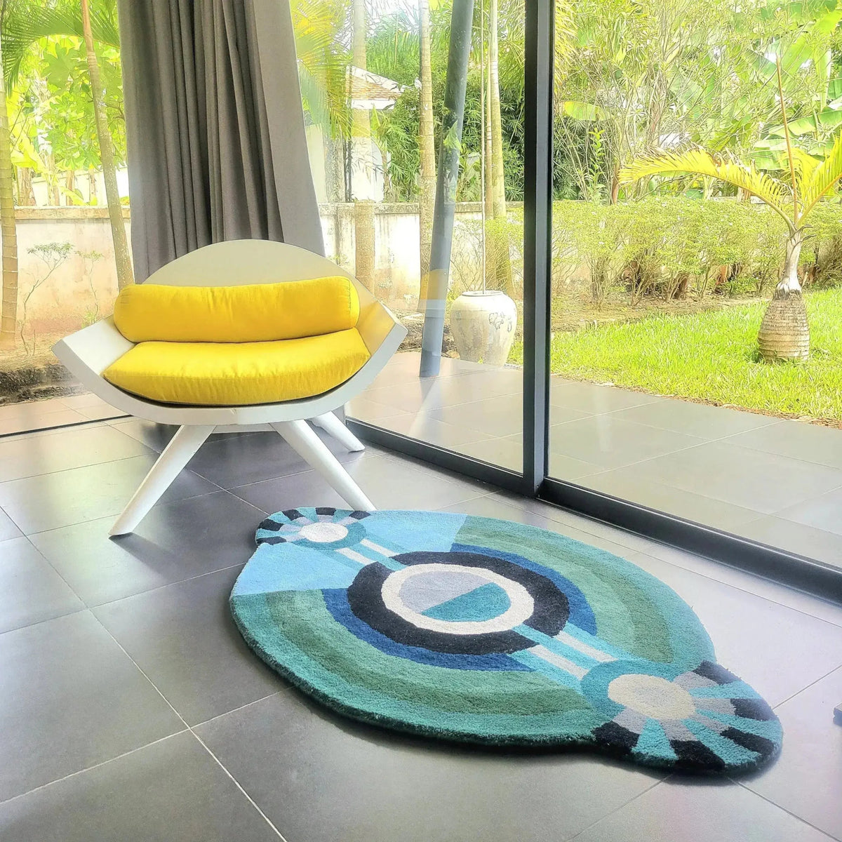 Colorful peacock feather-shaped rug on a tiled floor with a modern chair and glass door in the background.