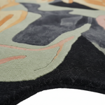 Close-up of an abstract area rug with a black border and a multicolor design featuring sage green, charcoal gray, peach, and beige organic shapes.