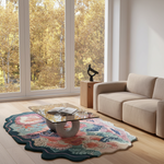 A modern living room scene featuring a highly decorative scalloped area rug with a colorful floral and botanical pattern, styled under a glass-top coffee table next to a beige sofa.