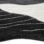 Close-up of a black textured rug with thin white pinstripes and a contrasting white section, showing the detailed pile texture.