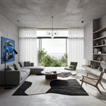 A modern, minimalist living room with a concrete ceiling and walls, featuring a gray sectional sofa, a blue car art print, a black and white abstract rug, and a large window overlooking a green outdoor landscape.