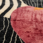 Close-up of a textured rug featuring a large dusty rose pink circular motif over a black background with cream-colored wavy stripes.