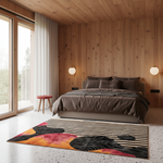 A modern bedroom with wood-paneled walls and ceiling, featuring a bed dressed in dark gray bedding, a colorful abstract area rug with black, pink, orange, and yellow tones, and large windows with white curtains.