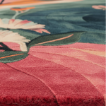 Close-up of a plush area rug with a floral and leaf pattern, showing textured pile in shades of pink, teal, green, and cream.