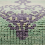 Close-up of a textured woven rug with a geometric medallion pattern in sage green and lavender purple.