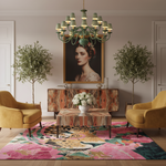 A styled living room interior featuring a large colorful area rug with a pink floral and leopard print, two mustard yellow armchairs, a marble-top coffee table, a marble credenza, and a green chandelier. A large framed portrait hangs on the wall behind the furniture.