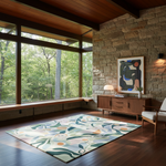 A rectangular area rug with a botanical and abstract pattern in muted green, beige, cream, and orange tones, styled in a modern rustic living room with a stone wall, wood floors, and a wooden console table.