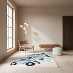 A modern living room scene featuring a rectangular area rug with an abstract botanical pattern in shades of teal, green, and black on a cream background. The room has light wood floors, a beige textured wall, a wooden chair, a floor lamp, a low wooden bench, and a white pouf.