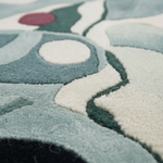 Close-up of a plush area rug with abstract organic shapes in pale blue, cream, dark green, and a small muted red accent.