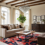 A styled living room interior featuring a beige sofa with brown and beige pillows, a wooden coffee table, a red and navy patterned rug, a dark wood sideboard, and a large crystal chandelier hanging from exposed wooden ceiling beams.
