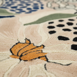 Close-up of a textured area rug with a floral pattern in cream, beige, orange, green, blue, and black.
