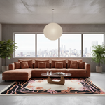 A modern sectional sofa in a warm rust-brown color, styled in a contemporary loft living room with a large floral area rug, a low wooden coffee table, and a large spherical pendant light. The room features a concrete ceiling and floor, large windows with a city skyline view, and potted plants.