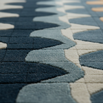 Close-up of a textured area rug with a modern geometric pattern of wavy, interlocking shapes in navy blue, slate blue, and cream.