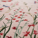 A close-up of a soft pink textile or rug featuring a delicate floral pattern with red flowers and green stems.