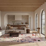 A modern living room with a light beige sectional sofa, a dark wood coffee table, a pink floral area rug, a wooden armchair, and a stone kitchen in the background.